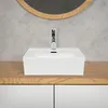 A white ceramic vessel sink with a chrome faucet is shown on a wooden countertop above white cabinets. A round mirror with a wooden frame is visible in the background. Produktbild-Vorschau
