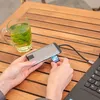 A person is using a USB hub with an SD card on a wooden table next to a glass of tea. Produktbild-Vorschau
