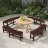 A circular wooden table and benches set up on a stone patio, surrounded by lush green foliage. Náhled obrázku produktu