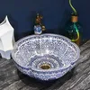 A decorative ceramic sink with a blue and white floral pattern sits on a dark countertop, with a faucet and a vase in the background. Náhled obrázku produktu
