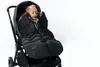 A baby wrapped in a black footmuff is sitting in a stroller against a white background. Náhled obrázku produktu