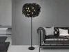 A black floor lamp with a feather-like shade is placed next to a black leather sofa in a modern living room. Voir les images du produit