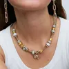 A close-up shot of a woman wearing a gold and silver charm necklace and matching earrings. Náhľad obrázku produktu