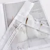 A close-up view of a white sheer curtain with decorative elements and text from a magazine in the background. Produktbild-Vorschau
