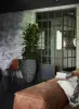 A modern living room with a brick wall, a large potted plant, a chair, and a leather sofa. Voir les images du produit