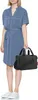 A woman is standing and holding a black bag. Produktbild-Vorschau