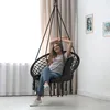 A woman is relaxing in a black hanging chair in a room with curtains and pictures on the wall. Voir les images du produit