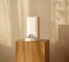 A cream-colored automatic pet feeder sits on a wooden pedestal against a textured wall. Produktbild-Vorschau