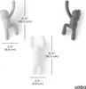 Three wall hooks shaped like stylized human figures are shown against a white background, with measurement indicators. Náhled obrázku produktu