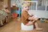 A young child is sitting on a potty in a nursery, reading a book. Produktbild-Vorschau