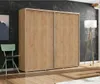 A spacious wardrobe with sliding doors is shown in a room with a dark textured wall, a green chair, and a floor lamp. Náhľad obrázku produktu
