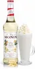A bottle of Monin White Chocolate syrup next to a glass of white chocolate drink with whipped cream. Podgląd zdjęcia produktu