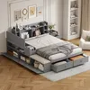 A bedroom setting with a large grey storage bed, complete with a bench and nightstand. The bed is made with white linens and a grey blanket. Produktbild-Vorschau