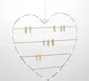 A heart-shaped wire frame with strings and clothespins, decorated with LED lights, hanging against a white background. Produktbild-Vorschau