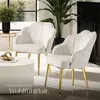 Two white velvet armchairs with gold legs are arranged in a living room setting with a coffee table and plants. Produktbild-Vorschau