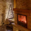 A decorative Christmas tree with lights and ornaments sits next to a fireplace with a fire burning. Náhled obrázku produktu