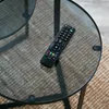 A remote control rests on a glass coffee table. Náhled obrázku produktu