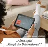 A person is relaxing on a couch, holding a tablet and listening to audio content. Produktbild-Vorschau