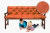 Two young boys are lying under a wooden bench with an orange cushion. Produktbild-Vorschau