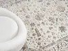 A close-up view of a rug with a floral pattern and a white chair. Produktbild-Vorschau