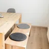 Two round felt seat cushions are placed on a wooden bench next to a wooden dining table. Produktbild-Vorschau