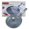 A frying pan with a glass lid is shown, with its packaging in the background. The packaging displays product information and imagery. Náhľad obrázku produktu