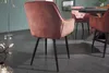 A close-up view of a pink velvet dining chair with black metal legs, placed in a dining room setting. Produktbild-Vorschau