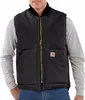 A man wearing a black Carhartt vest over a grey long-sleeved shirt and blue jeans.