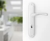 A close-up of a silver door handle on a white background, with a blurred interior scene in the background. Produktbild-Vorschau