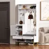 A white entryway cabinet with a bench and shoe storage, placed next to a dark door and a sofa. Produktbild-Vorschau