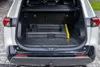 The open trunk of a white car with a black rubber mat. A folded black plastic item is placed on the mat, with a yellow strap leaning against it. Produktbild-Vorschau