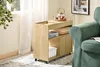 A wooden rolling cart with storage compartments is placed next to a green armchair in a room with natural light coming from a window. Podgląd zdjęcia produktu