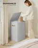 A woman is putting clothes into a grey laundry basket with a lid. Produktbild-Vorschau