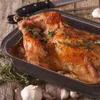 A roasted chicken in a roasting pan on a wooden surface, with garlic and herbs. Produktbild-Vorschau