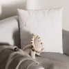A white pillow with a wavy pattern and a stuffed lion toy are placed on a gray sofa with a knitted blanket. Produktbild-Vorschau