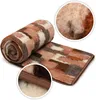 A rolled-up and unrolled wool blanket with a camouflage-like pattern of brown, white, and gray patches. Close-up insets show the texture of the wool and the stitched edge of the blanket. Produktbild-Vorschau