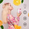 A woman holding a product container with oranges and leaves around her. Produktbild-Vorschau