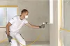 A man is using a paint sprayer in a room. Produktbild-Vorschau
