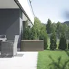 A brown plastic storage box sits on a patio next to a grey wicker chair, with green grass and trees in the background. Náhled obrázku produktu