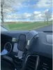 A car's dashboard with a phone holder mounted on it, with a view of a rural landscape through the windshield. Anteprima dell’immagine prodotto