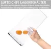 A hand is holding a clear plastic food storage container filled with water and two orange spheres, likely demonstrating its use. Produktbild-Vorschau