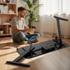 A man is assembling a black desk in a room with a bookshelf and a plant. Produktbild-Vorschau