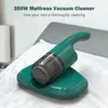 A green handheld mattress vacuum cleaner is placed on its charging base on a white bed. There is a lamp on the left. Náhled obrázku produktu