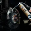 A gloved hand sprays brake cleaner onto a car's brake rotor and caliper. Produktbild-Vorschau
