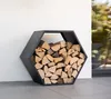A hexagonal black metal log holder filled with firewood, leaning against a white wall outdoors. Podgląd zdjęcia produktu