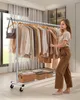 A woman is standing next to a rolling garment rack filled with clothes, sorting through them. Produktbild-Vorschau