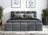 A modern bedroom setting with a gray upholstered bed, pillows, and two potted plants. Produktbild-Vorschau