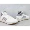 A pair of white and gray Adidas Hoops 3.0 Mid sneakers are displayed on a light gray, textured surface. Produktbild-Vorschau