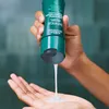 A hand holding a bottle of Aveda Botanical Repair shampoo, dispensing it into the palm of another hand. Anteprima dell’immagine prodotto