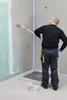 A person is applying a waterproofing compound to a wall with a roller in what appears to be a bathroom construction or renovation. Produktbild-Vorschau